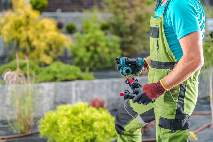 landscaper holds irrigation parts standing over flower bed