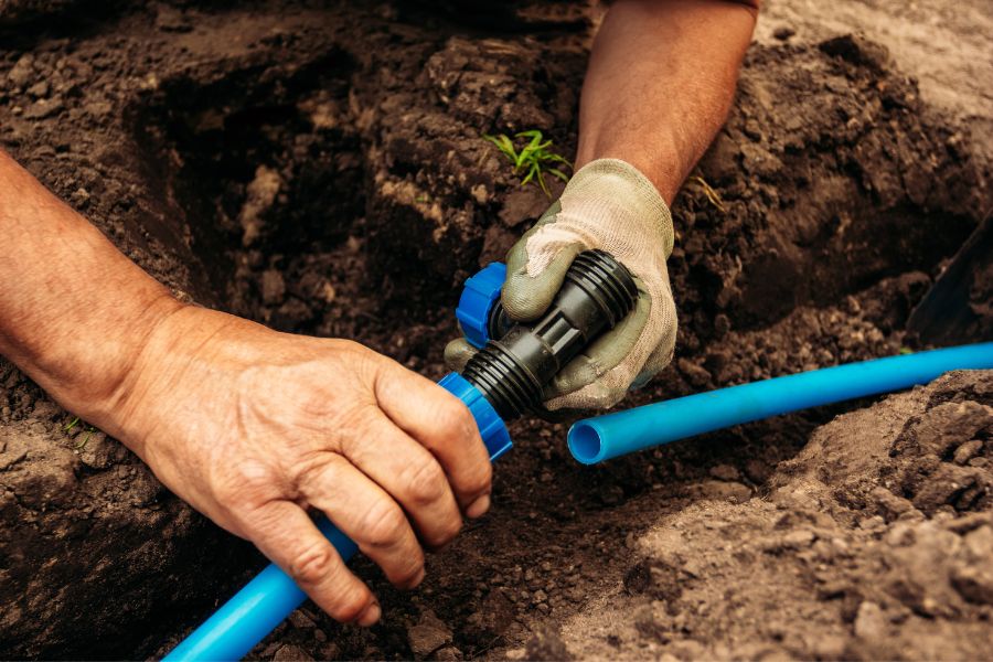 someone wearing work gloves holds a irrigation line in the ground