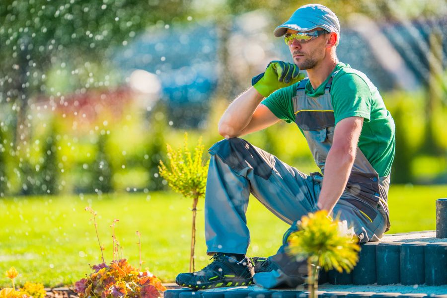 worker sits on patio while sprinklers water landscaping around them